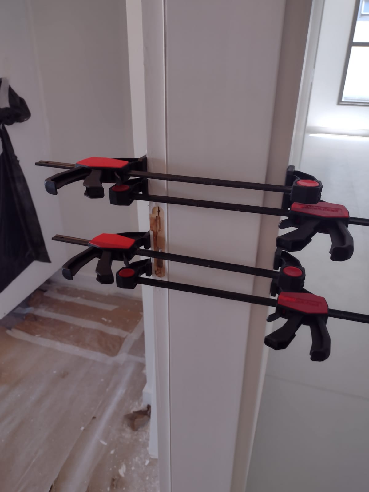 Reparo de porta de madeira em andamento, fixada com sargentos durante a colagem